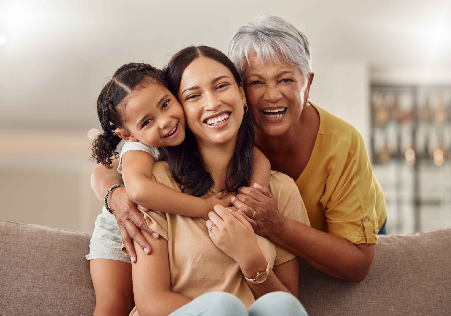 Grandmother, mom and child hug in a portrait for mothers day on a house sofa as a happy family in Colombia. Smile, mama and elderly woman love hugging young girl or kid and caring for aging parents.