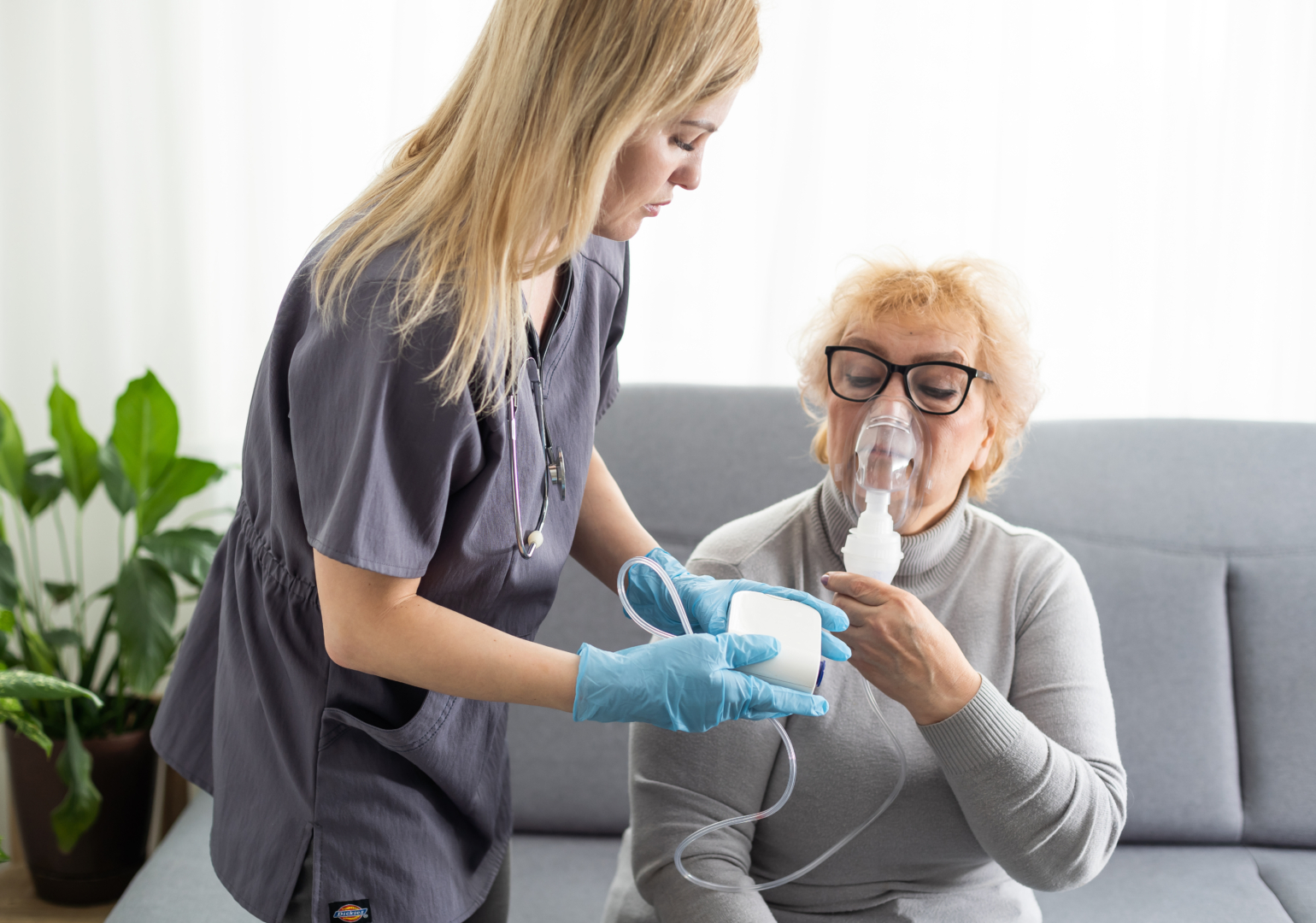 Young girl doctor makes inhalation to an older woman on a white background. Fights chronic respiratory conditions at home.